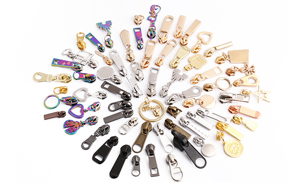 Assorted custom zipper pullers in various shapes, colors, and finishes including metal, plastic, and rainbow designs